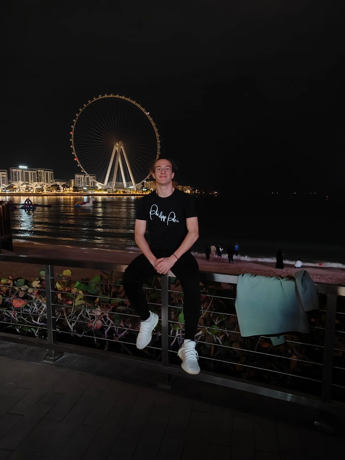 Ivan Vojvoda sjedi na ogradi šetnice u Dubaiju, iza njega osvijetljeni panoramski kotač Ain Dubai